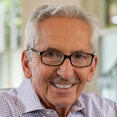A smiling person with gray hair and glasses wearing a checkered shirt, captured in a head-and-shoulders portrait.