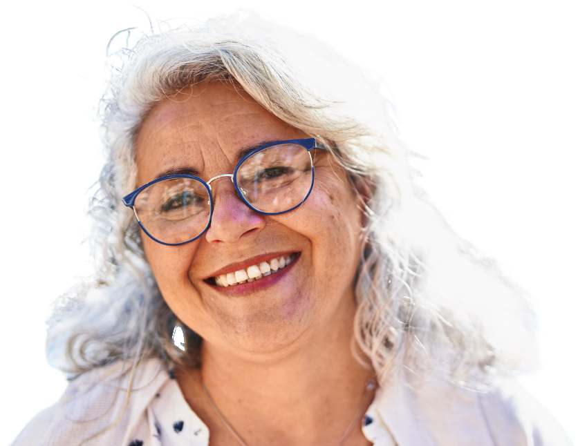 A smiling person with wavy gray hair wearing dark-rimmed glasses and a white patterned shirt with a necklace.
