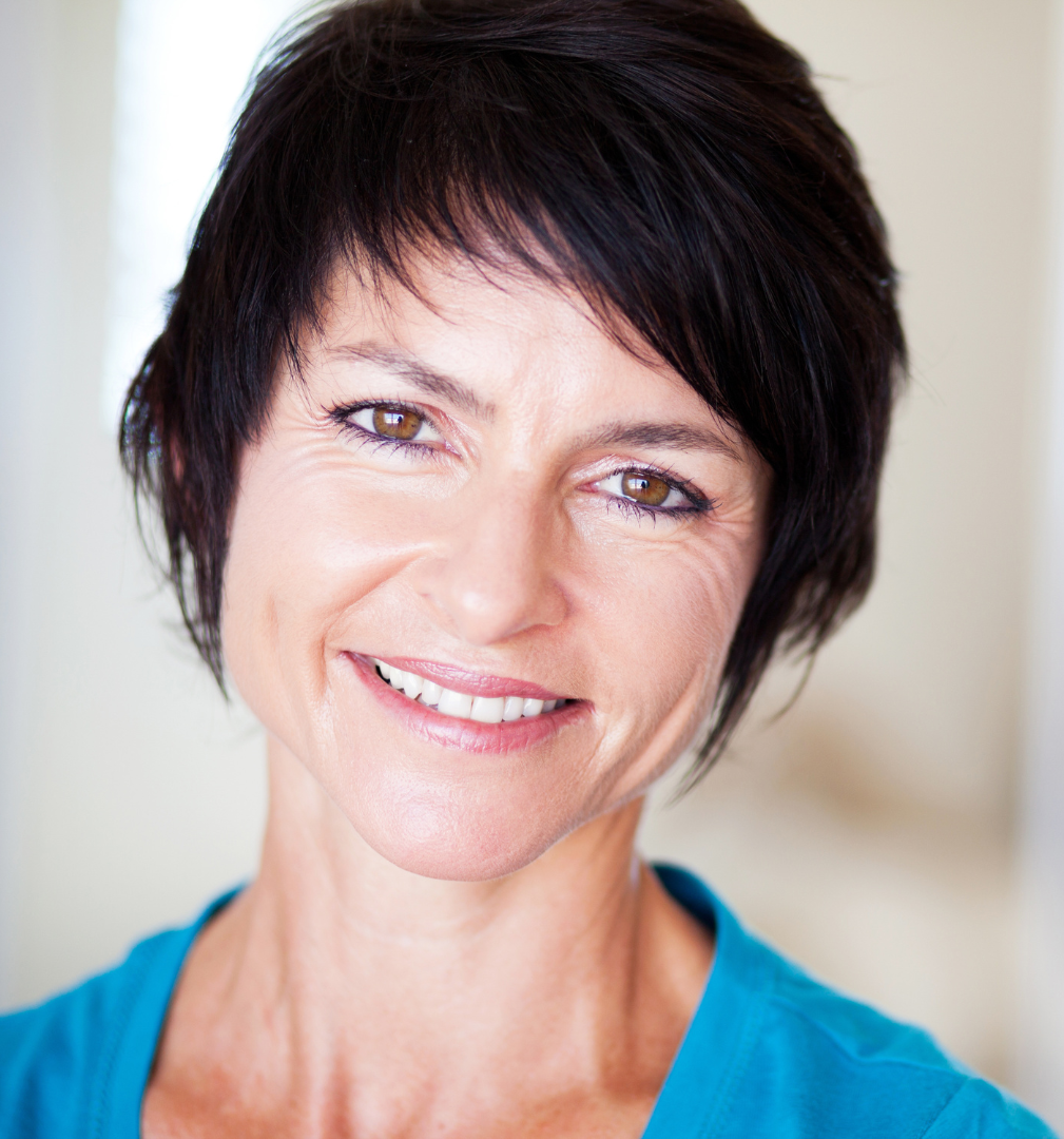 A smiling person with short, dark hair wearing a bright blue top against a light, neutral background.