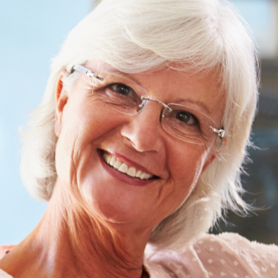 A smiling person with white hair and glasses looking toward the camera.