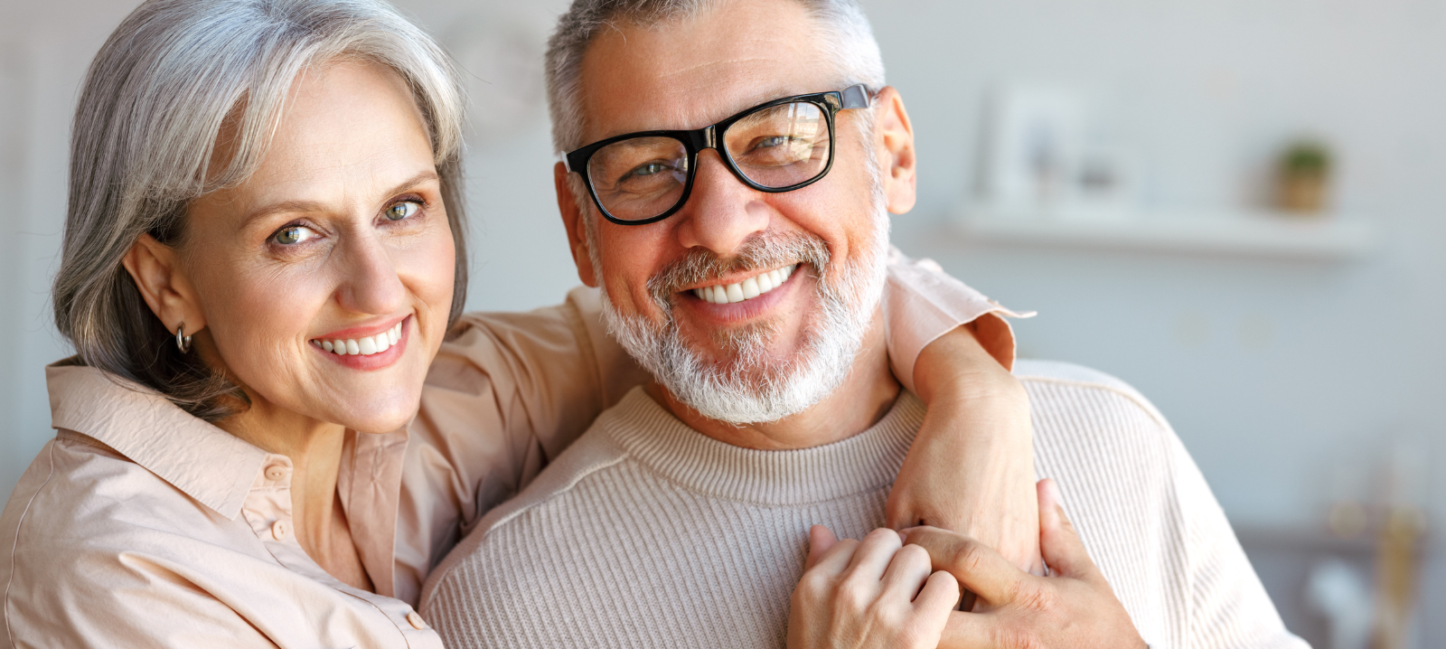 A smiling couple embraces closely, looking at the camera in a brightly lit indoor space.