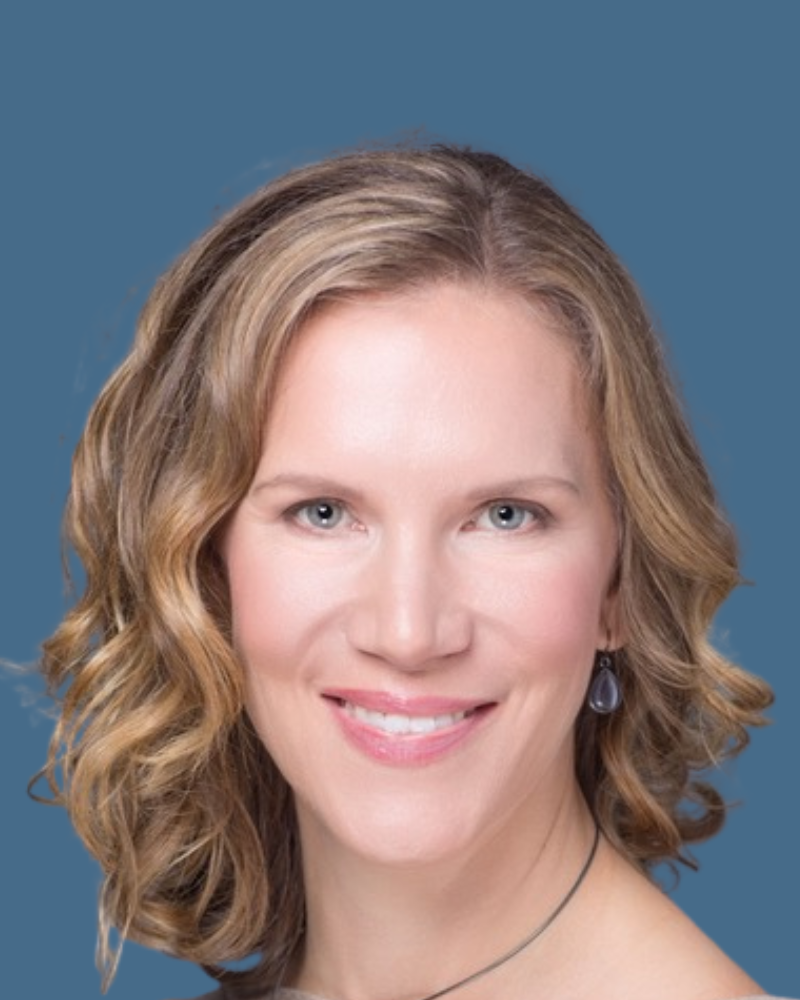 Headshot of a smiling person with wavy brown hair wearing small, dark, teardrop-shaped earrings against a blue background.