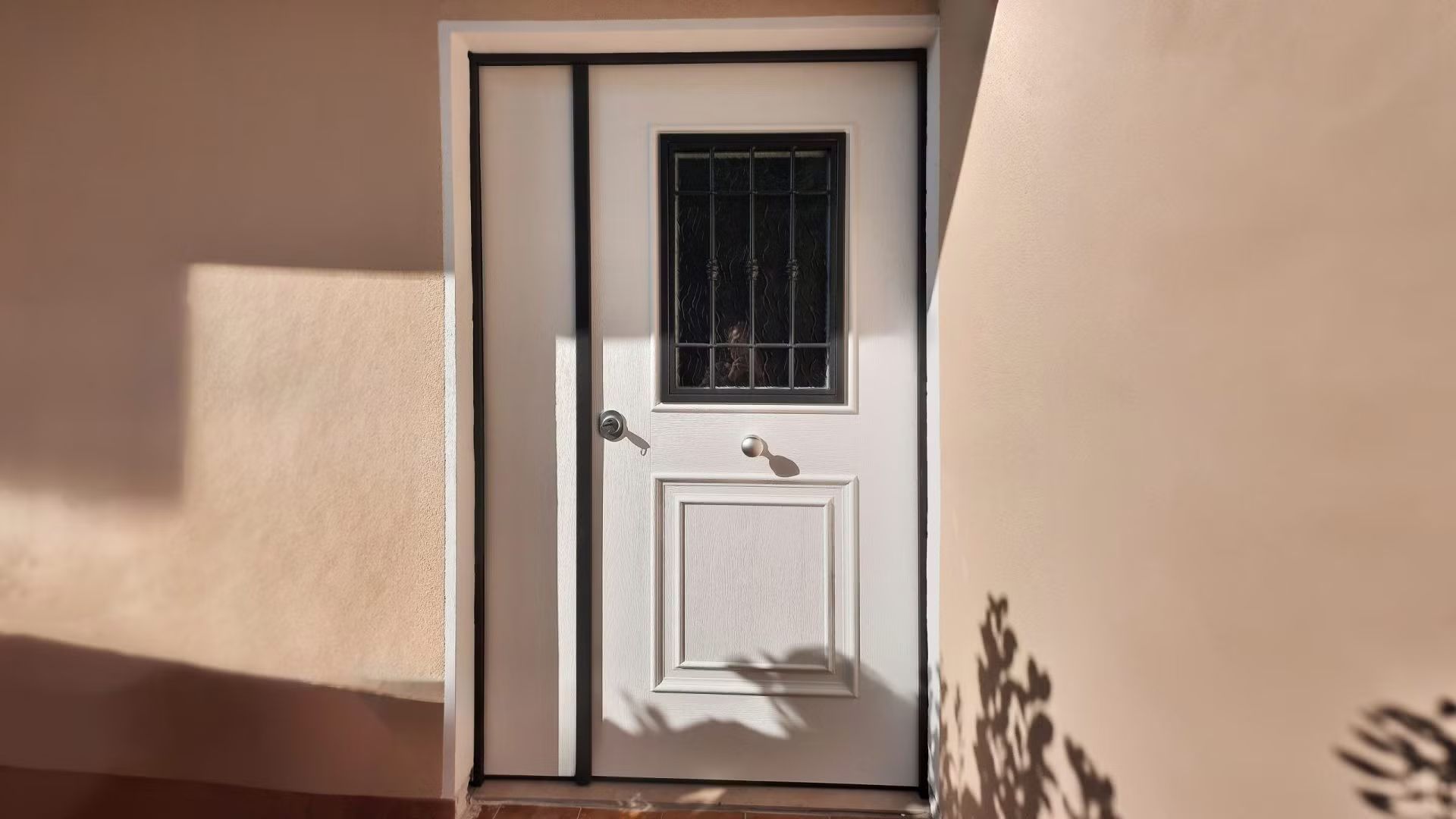 Una porta bianca con una finestra nera e un'ombra sul muro.