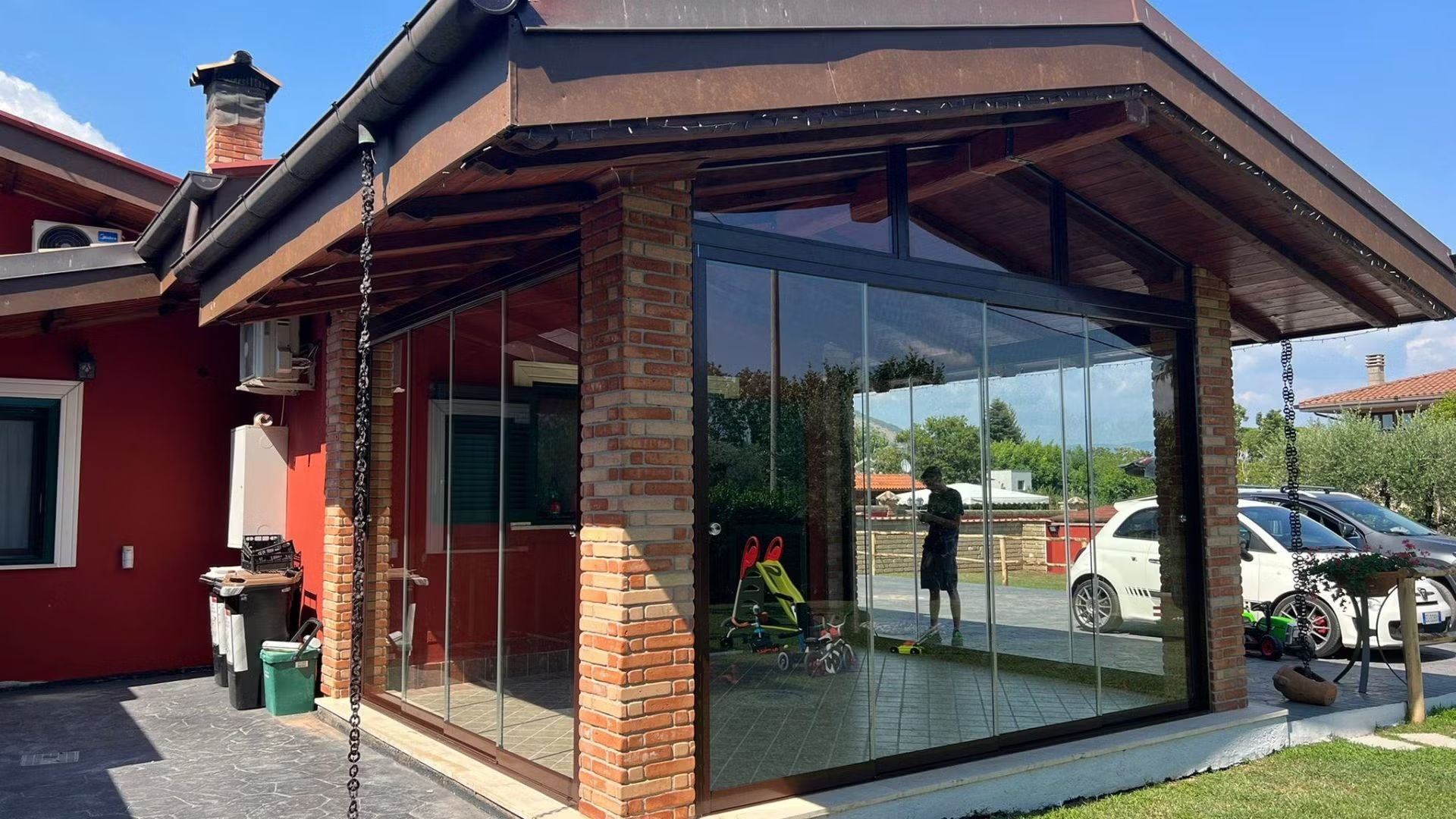 Una casa rossa con un grande portico in vetro e un'auto parcheggiata davanti.