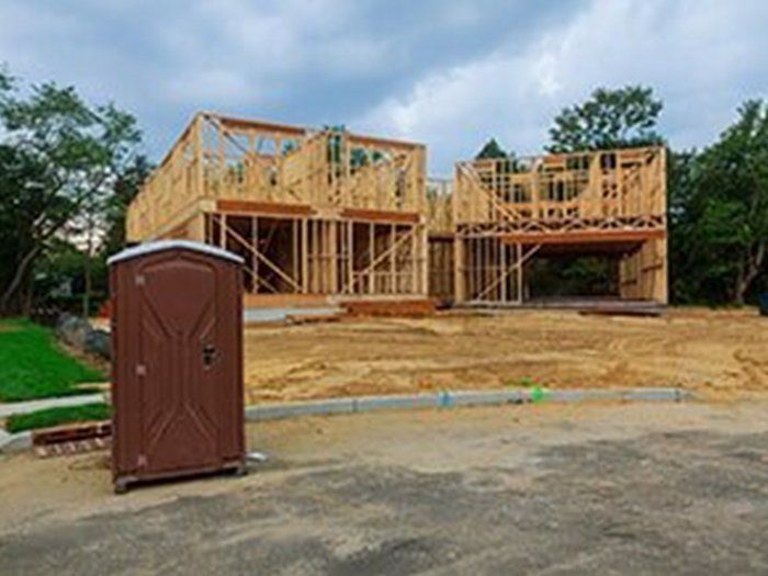 Wooden frame of a house under construction with a portable toilet in front.