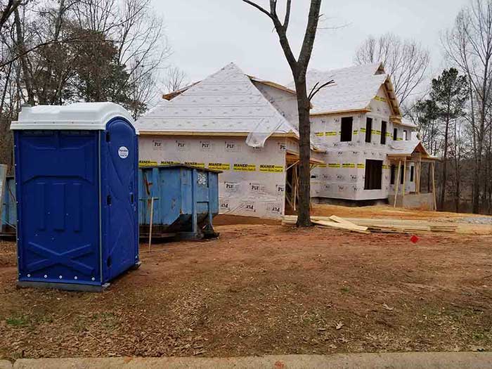 Blue portable toilet and construction site of a new house with lumber and wrap visible.