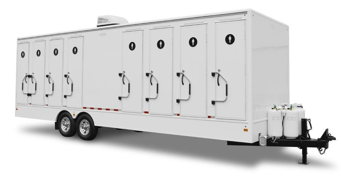 White portable restroom trailer with multiple stalls, on a trailer.