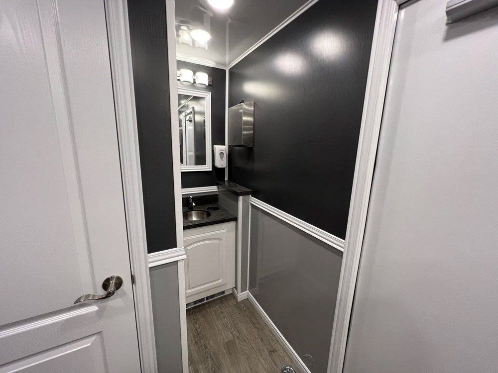 Interior of a portable restroom with a sink, mirror, and black and gray walls.