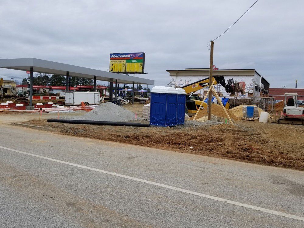 Construction site with gas station canopy, portable toilet, and equipment on a cloudy day.
