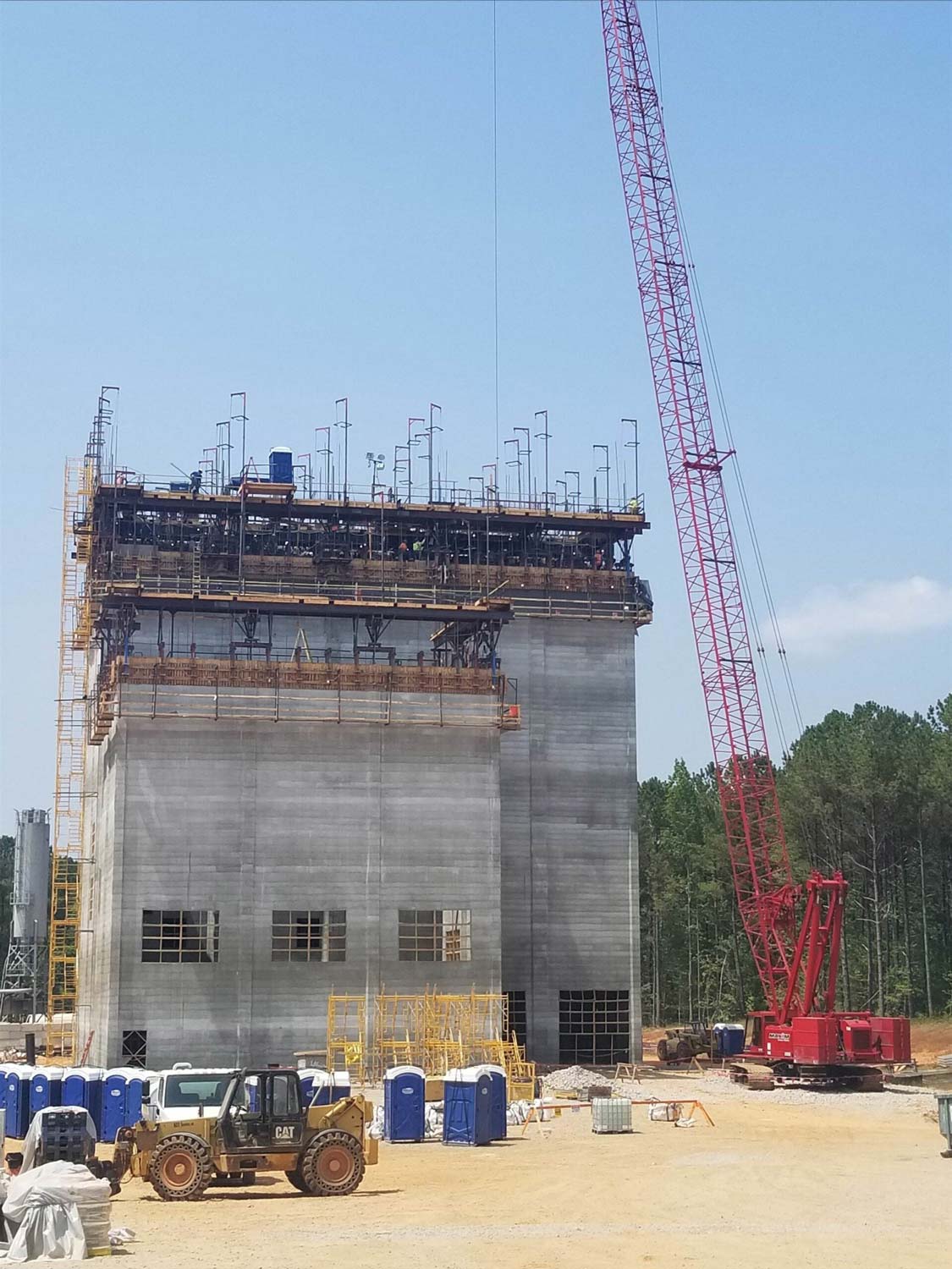 Construction site with a tall concrete building under construction, red crane, and blue portable toilets.