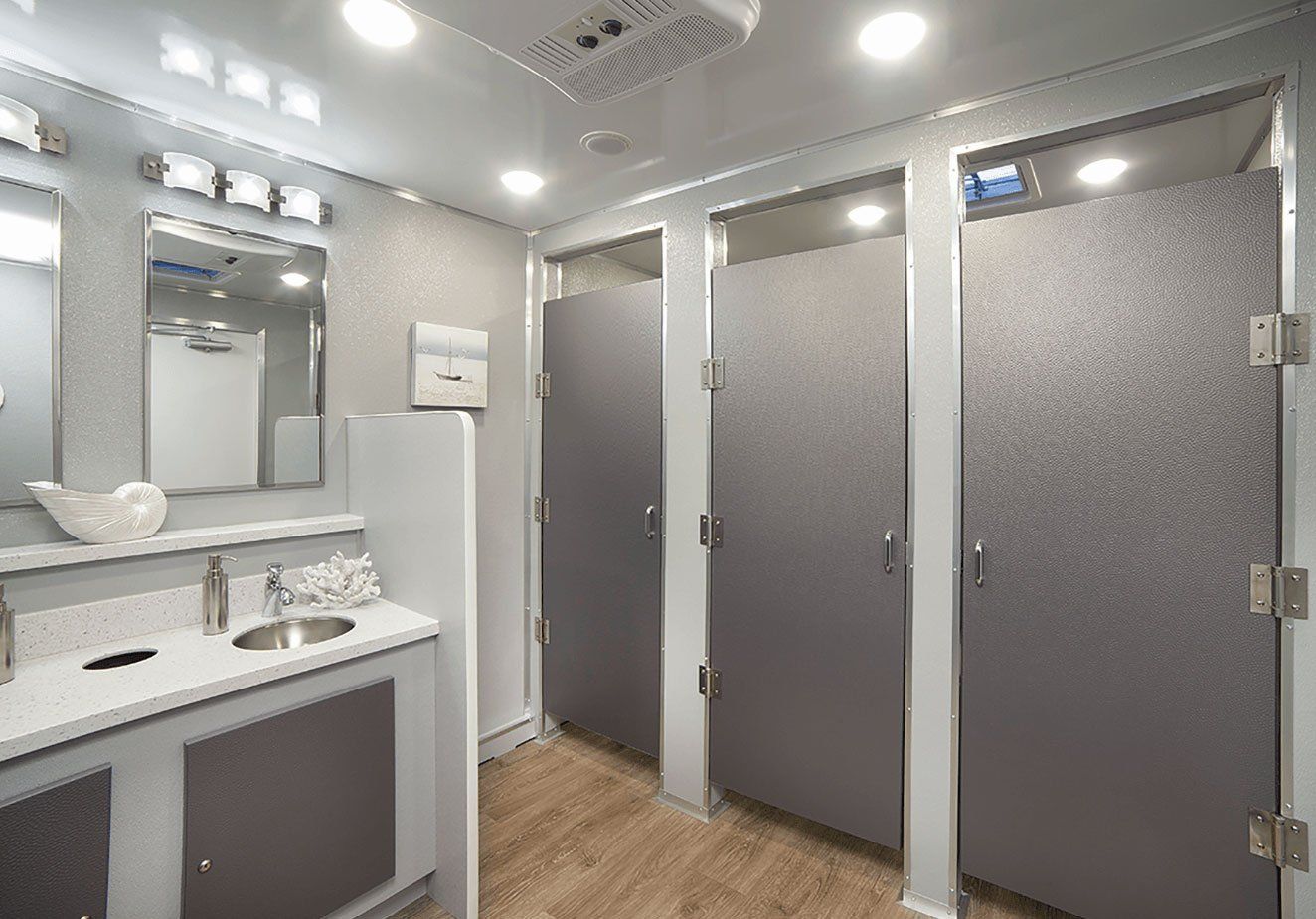 Interior of a mobile restroom unit with stalls, mirrors, sinks, and overhead lighting.