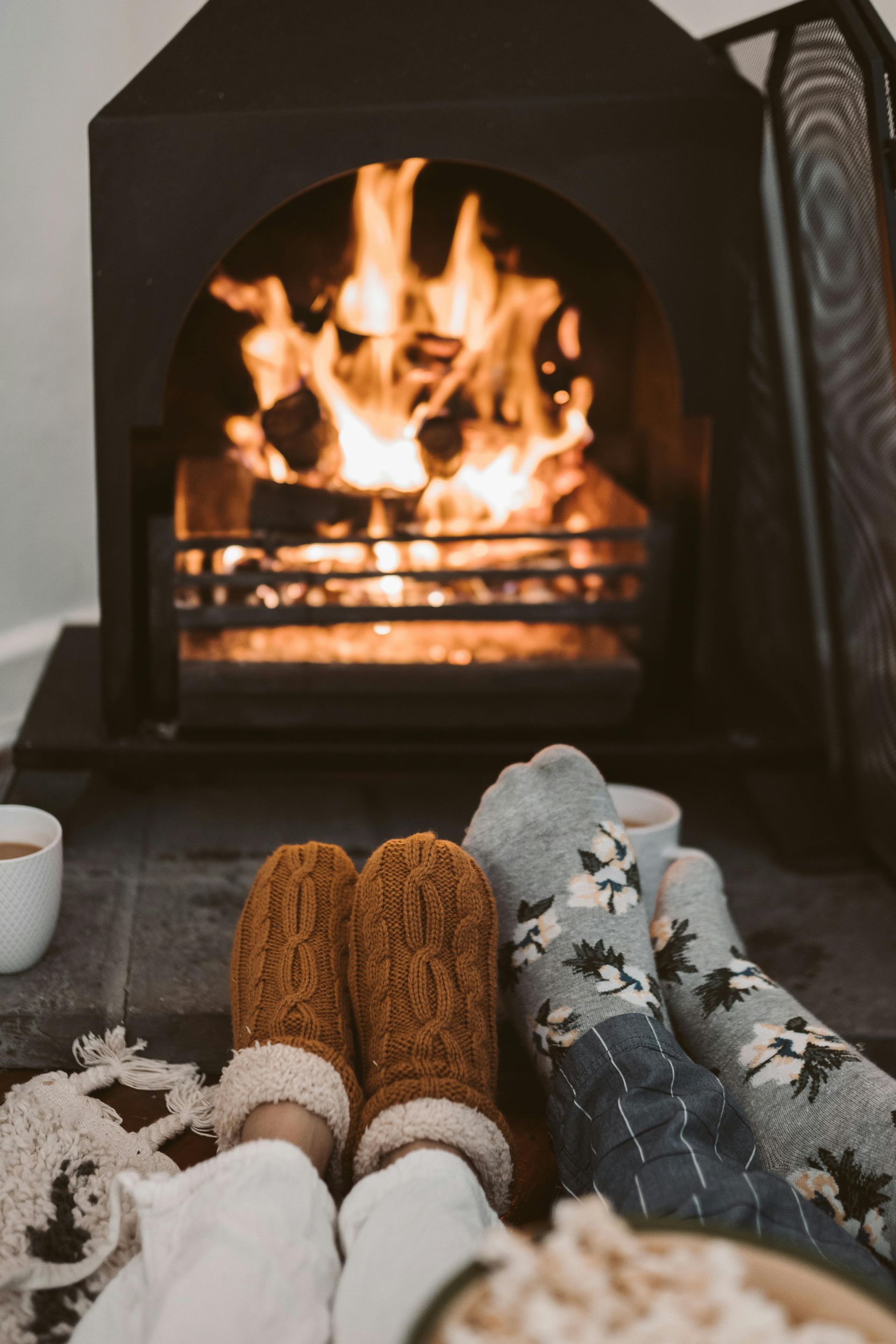 People wearing mittens and socks by a fireplace.