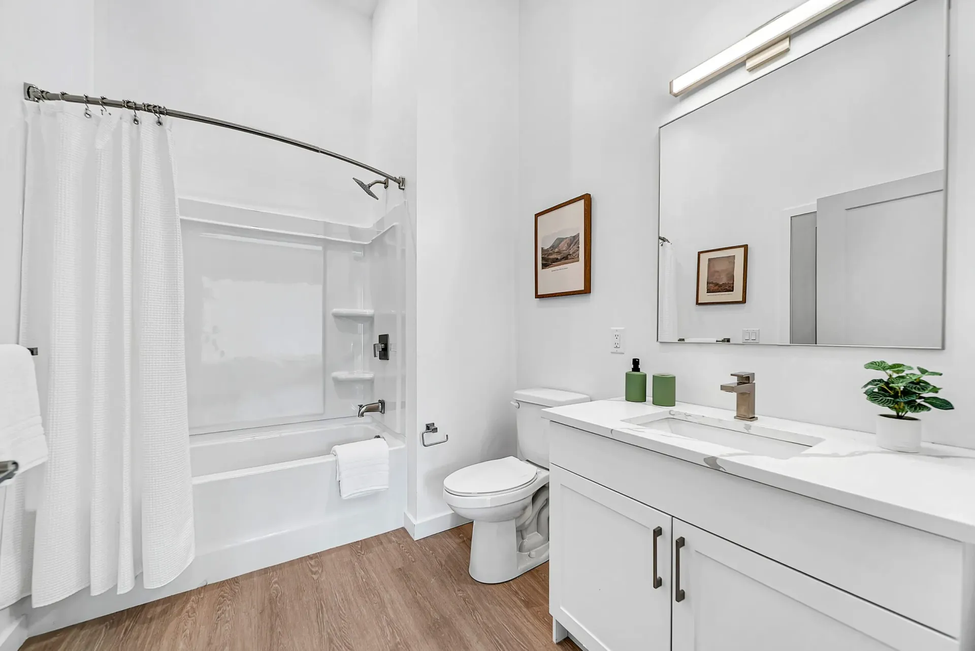 Modern white bathroom with a bathtub, shower, toilet, and vanity with a large mirror.