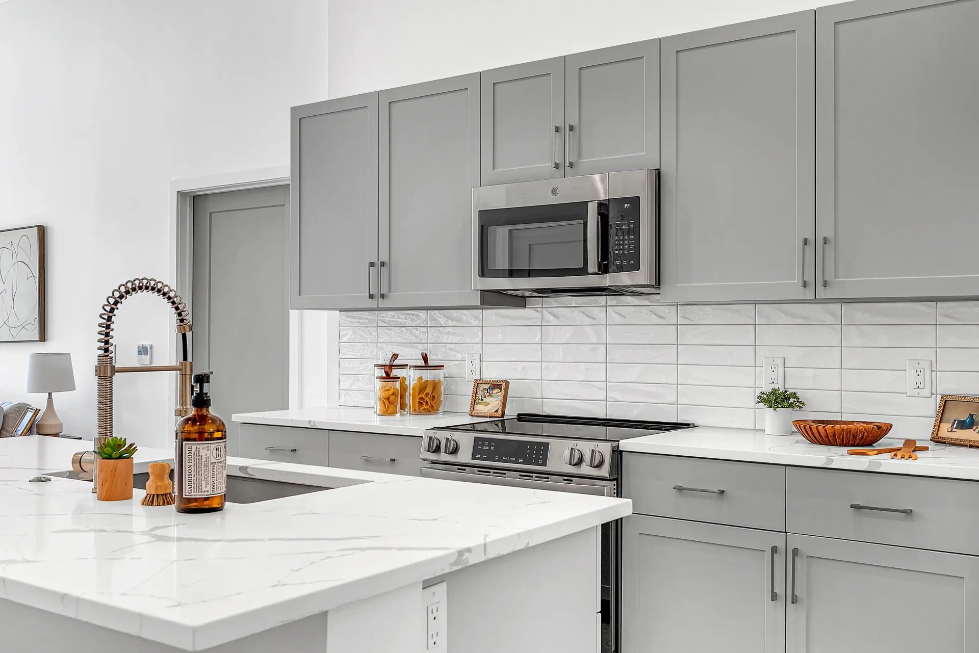Modern kitchen with gray cabinets, white quartz countertops, stainless steel appliances, and subway tile backsplash.