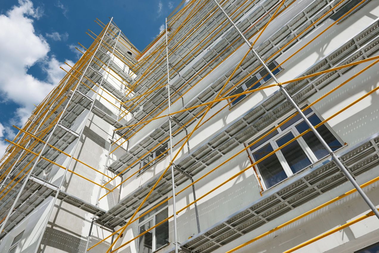 Vista dal basso di un edificio bianco in costruzione con impalcature gialle sullo sfondo di un cielo blu.