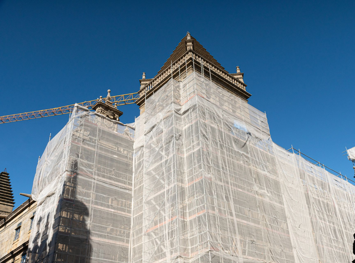 Edificio in costruzione ricoperto di impalcature sullo sfondo di un cielo azzurro limpido.