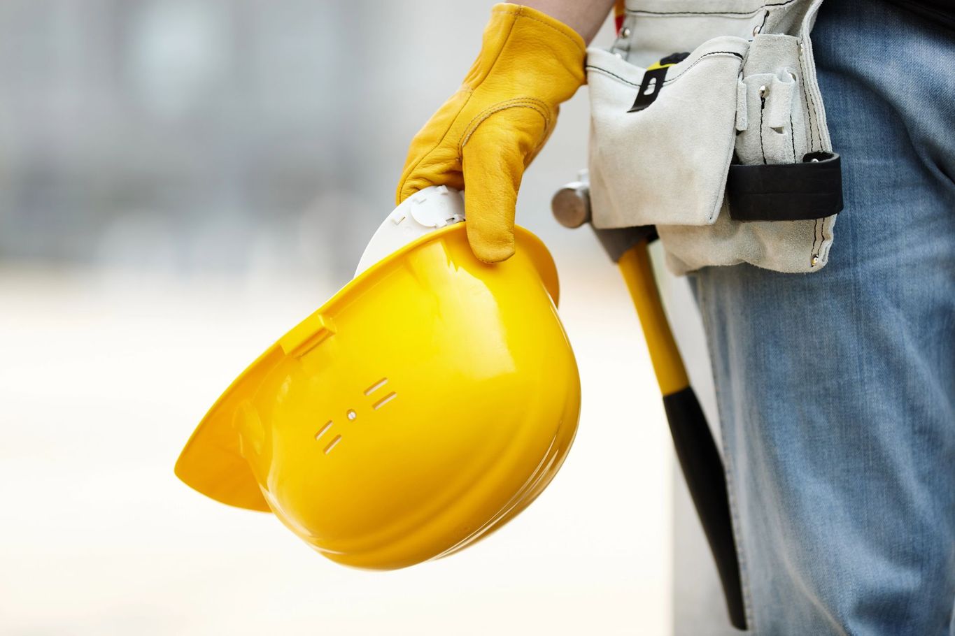 Operaio edile con elmetto giallo e attrezzi in un cantiere.