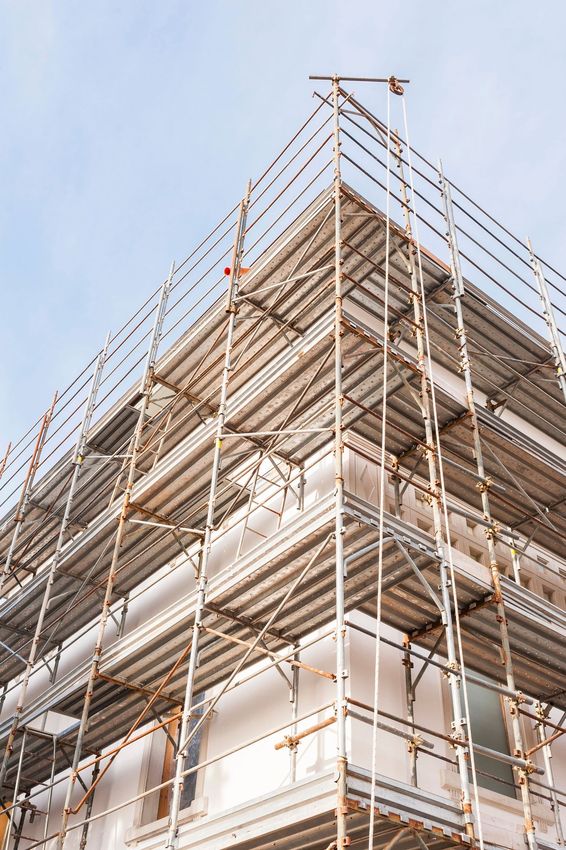 Impalcature attorno a un edificio a più piani in costruzione, viste dal basso contro un cielo azzurro.