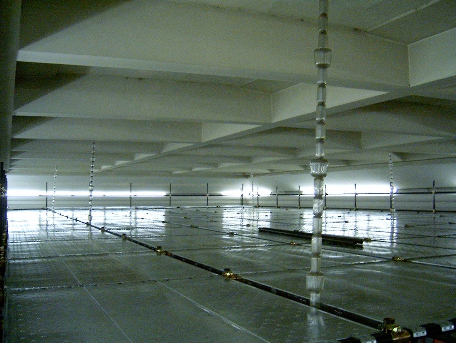 Parcheggio industriale vuoto con pilastri e travi a vista in cemento, illuminato dalla luce naturale proveniente dall'estremità opposta.