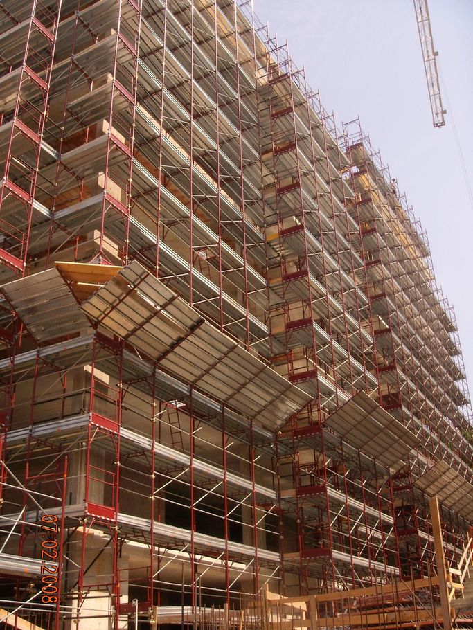 Edificio a più piani in costruzione con impalcature e operai su una gru.