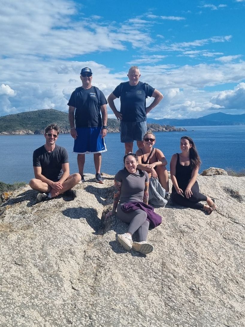 A group of people are posing for a picture on top of a rock overlooking the ocean.