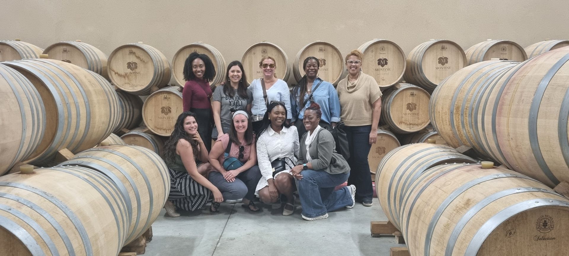 A group of people are posing for a picture in front of a stack of wine barrels.
