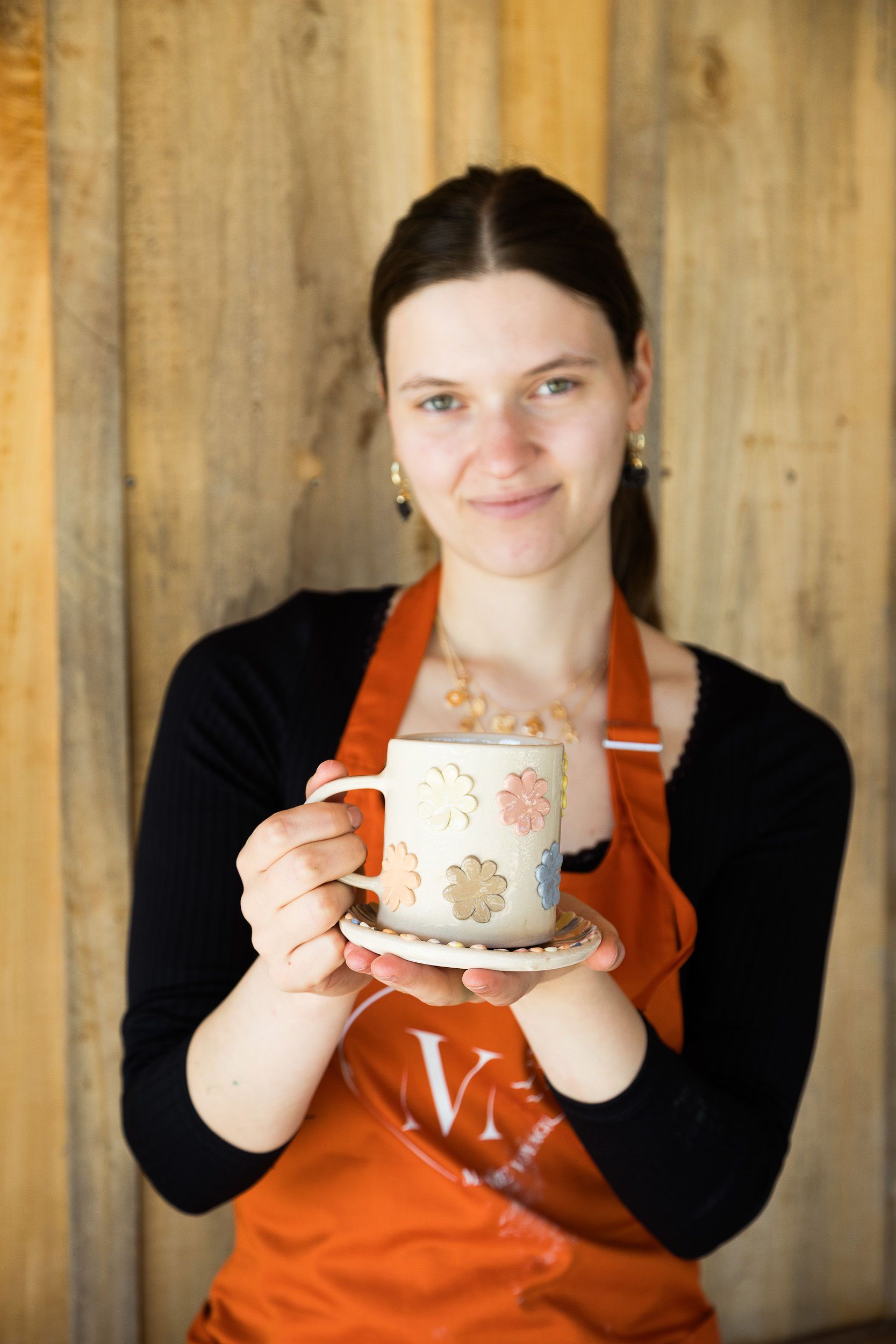 A woman in a colorful dress is standing in front of a shelf full of mugs.