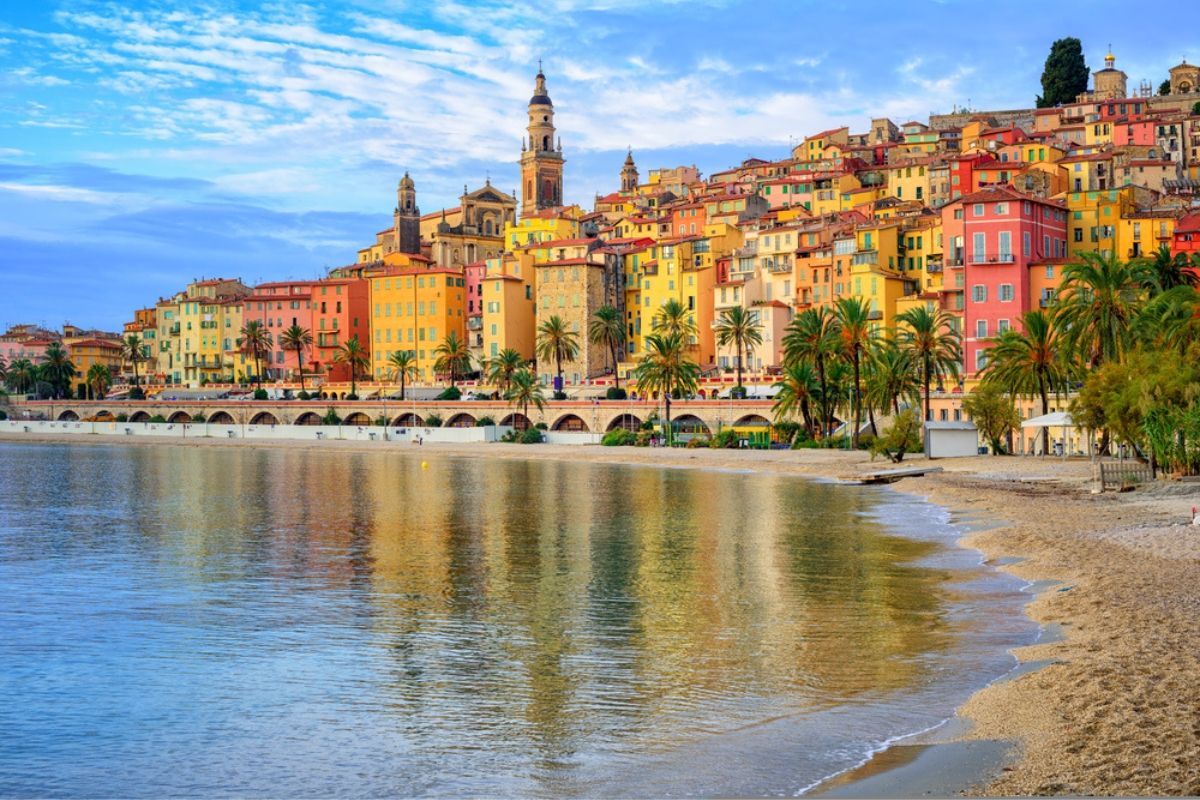 A beach with a city in the background and a body of water in the foreground.