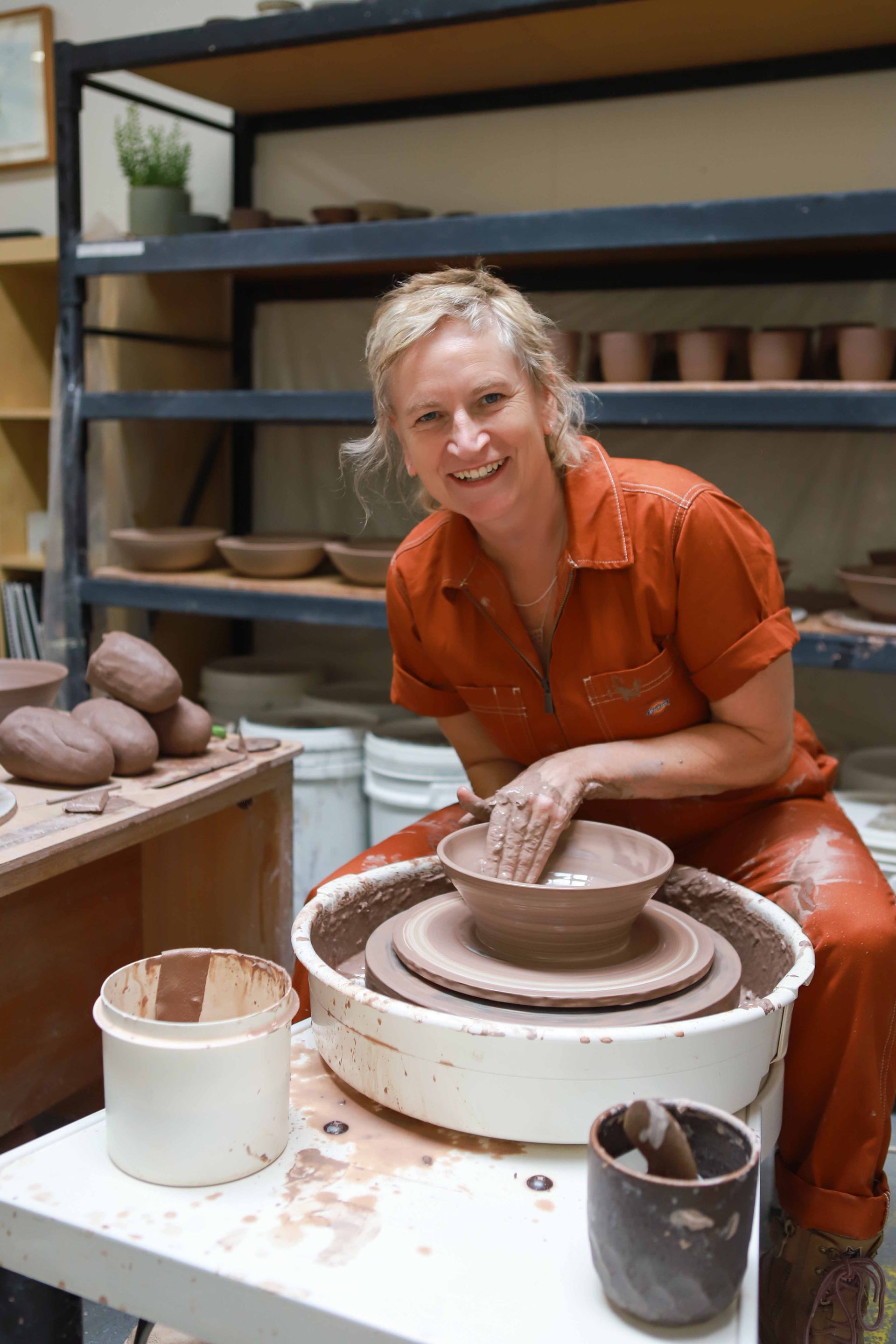 A woman is sitting on a pottery wheel making a bowl.