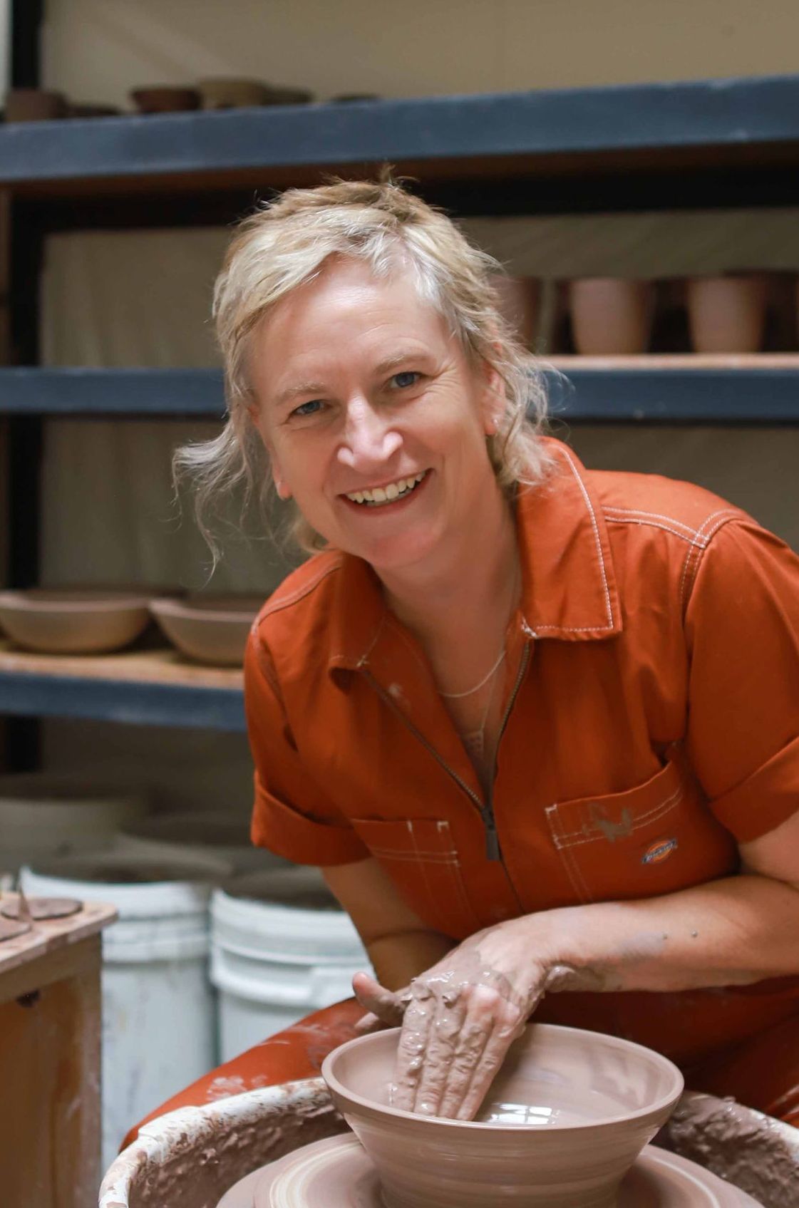 A woman is sitting on a pottery wheel making a pot.