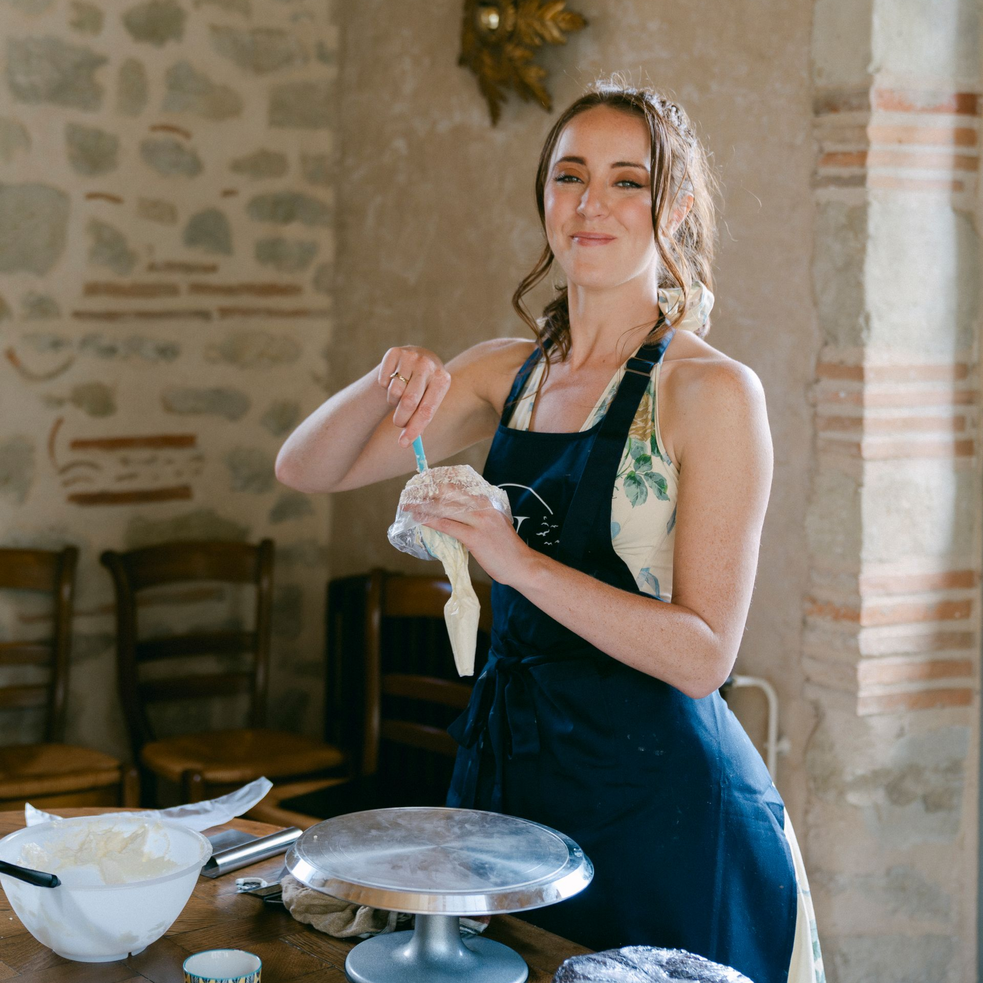 A woman in a yellow jumpsuit is sitting next to a yellow cake.
