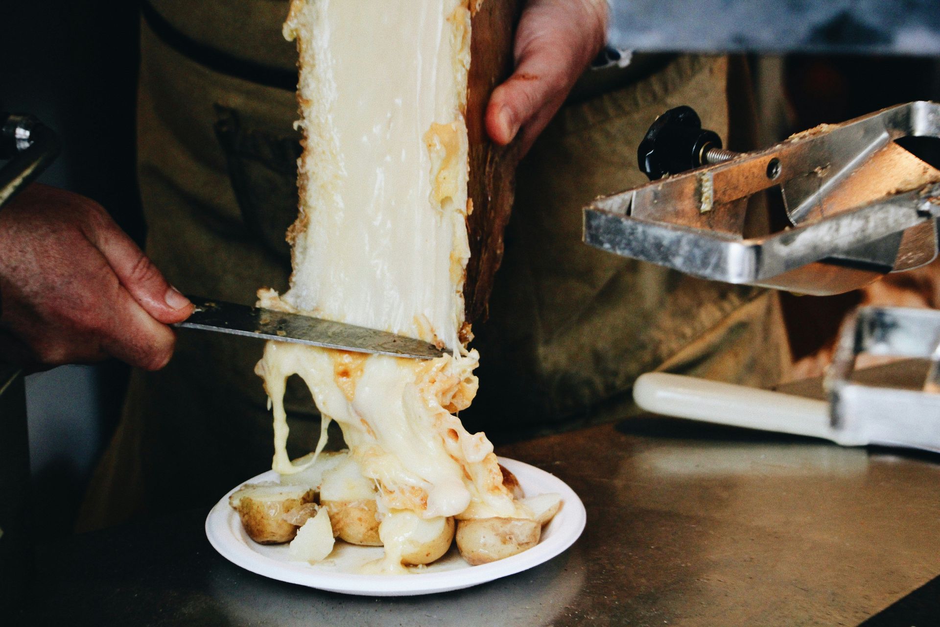 A person is cutting a piece of cheese on a plate.