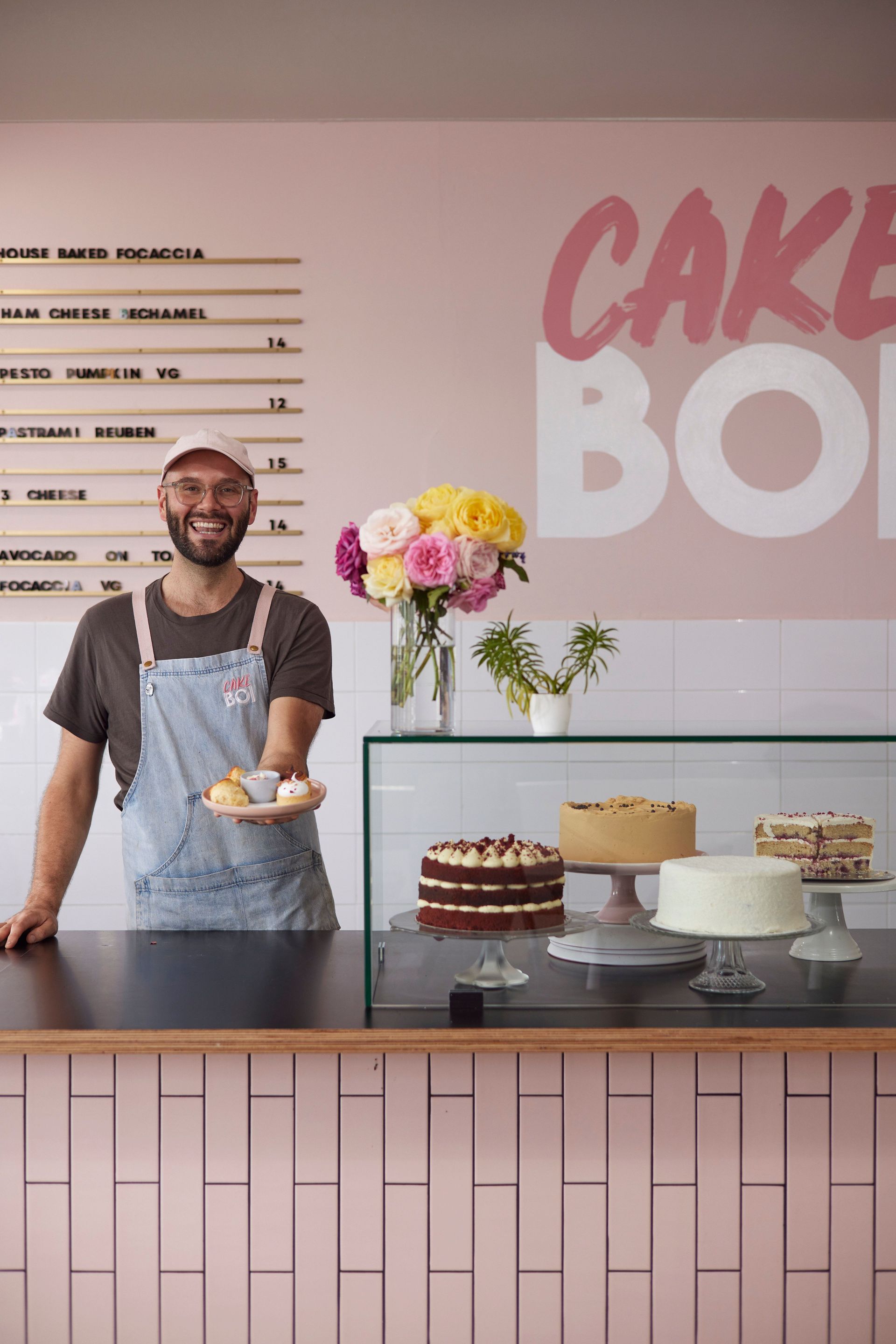 A man is standing behind a counter in a bakery holding a plate of food.