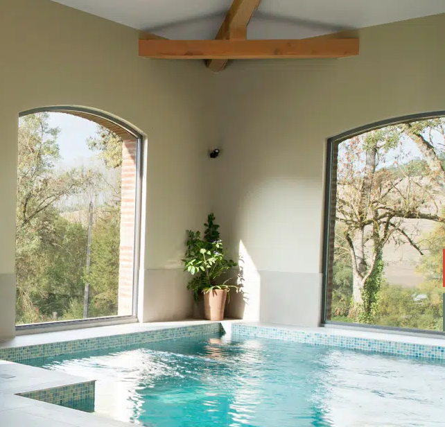 A large indoor swimming pool surrounded by windows and trees