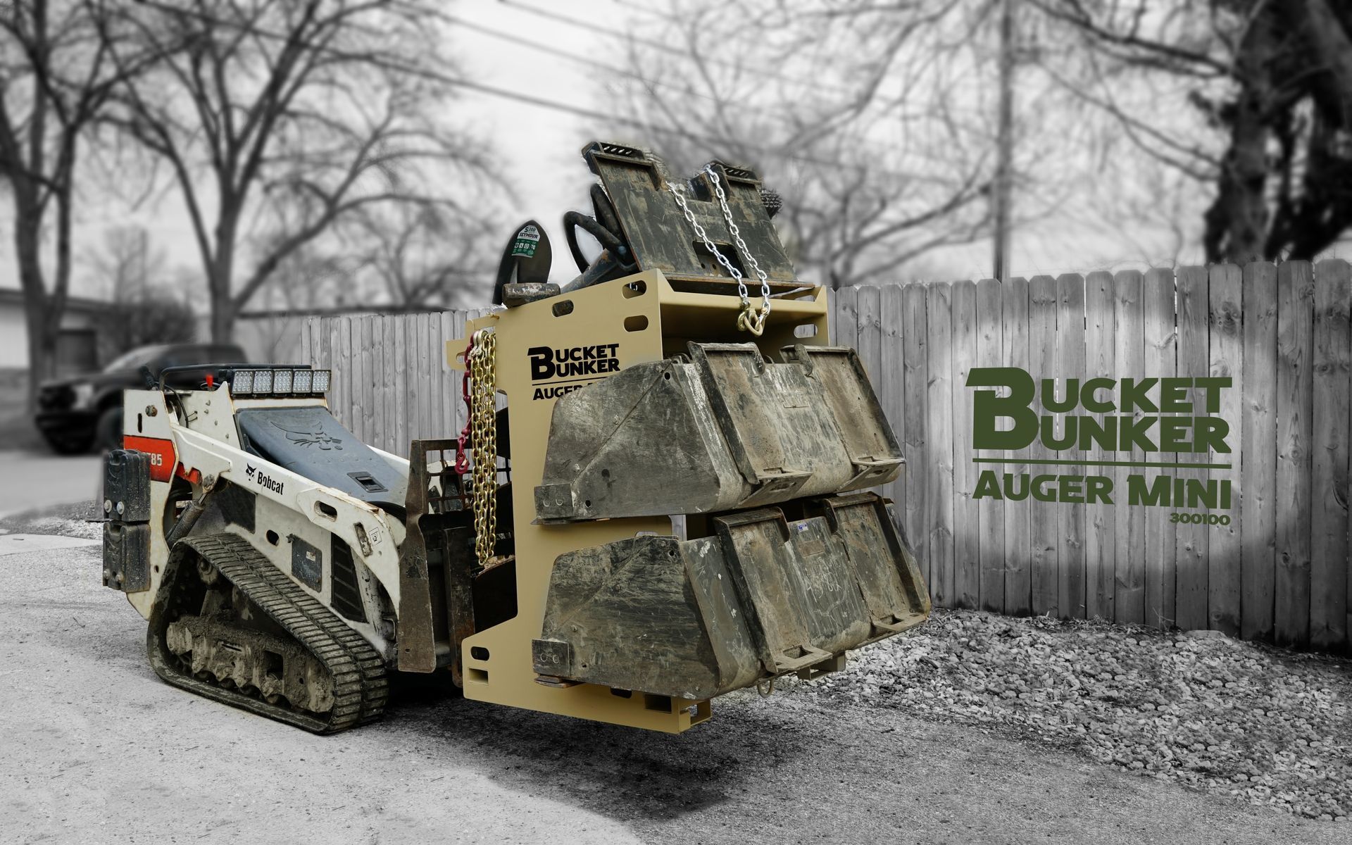 A bucket bunker auger mini is parked in front of a wooden fence