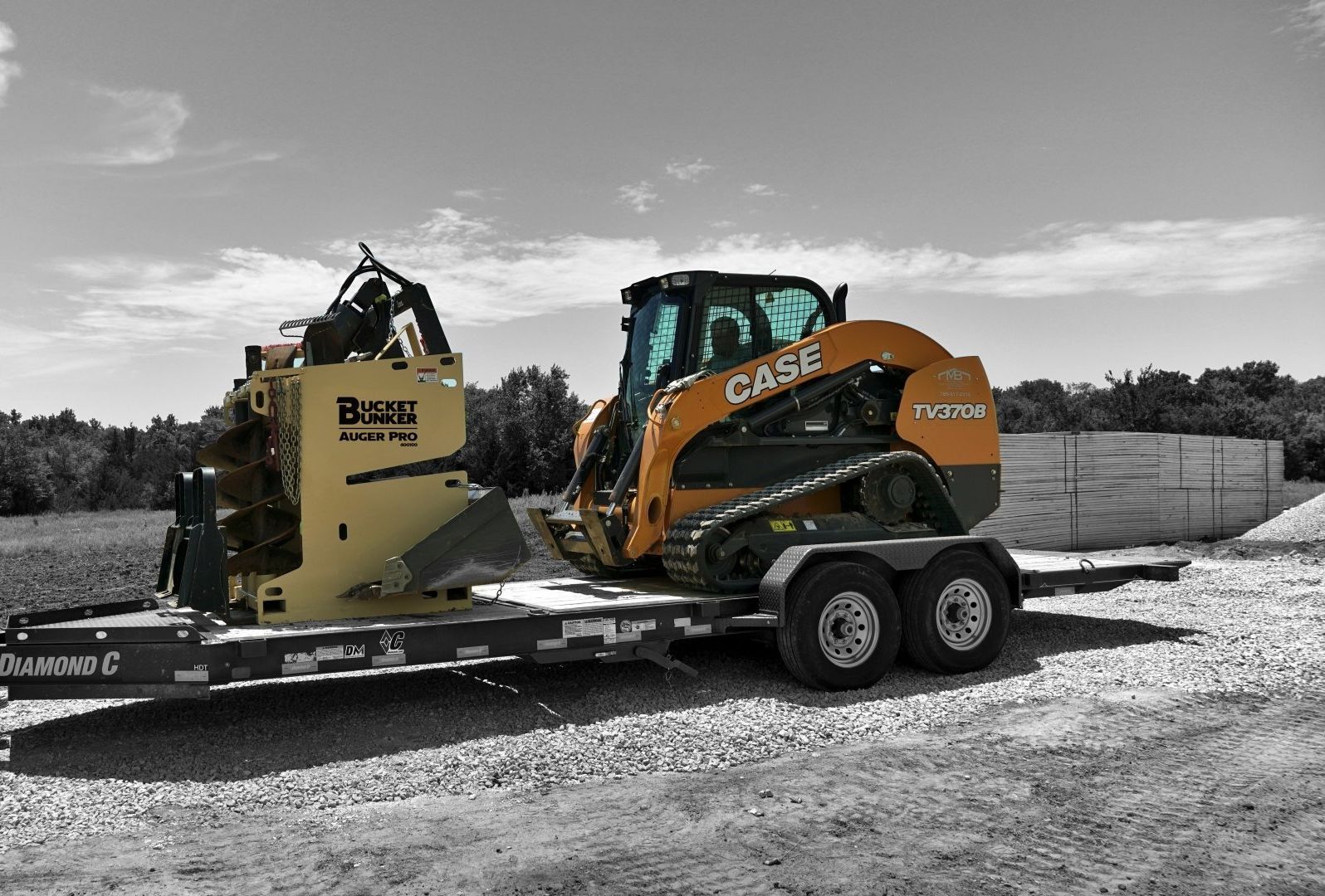 A black and white photo of a bucket bunker with attachments on a trailer with a case skid steer. 