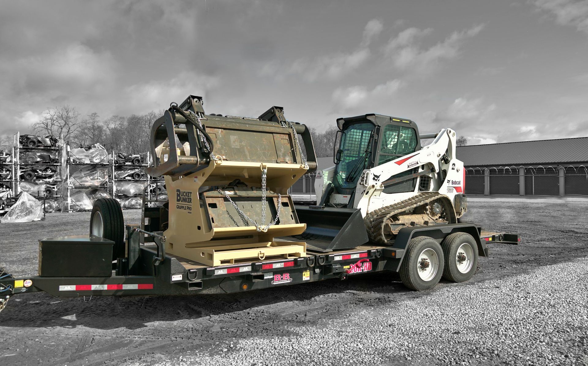 A black and white photo of a bucket bunker with attachments on a trailer with a bobcat skid steer. 