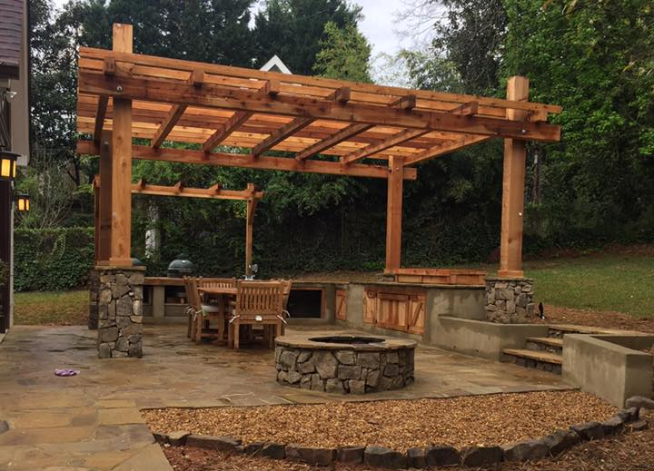 There is a fire pit in the middle of the backyard under a pergola.