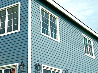 Blue house siding with white-trimmed windows and corner trim under a pale sky