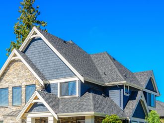 Modern house with gray shingle roof and blue siding against a bright blue sky