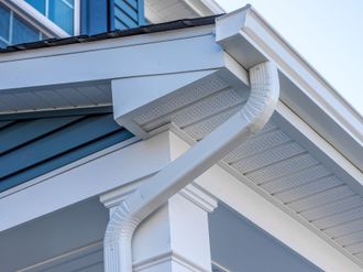 White rain gutter and downspout on a blue house roof corner