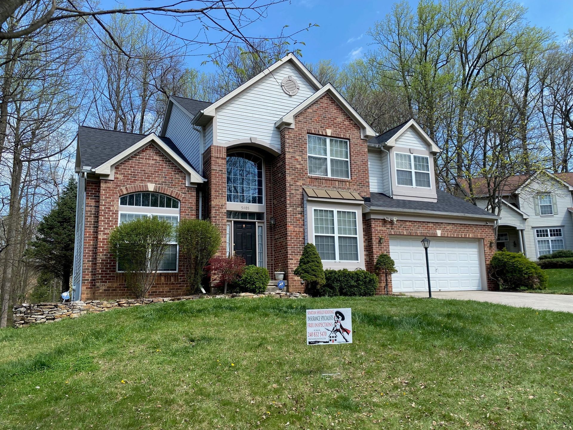 Two-story brick and white suburban house with a front lawn and a for-sale sign