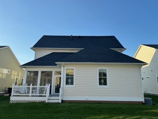 White two-story house with a front porch, beige siding, and dark roof under a clear blue sky