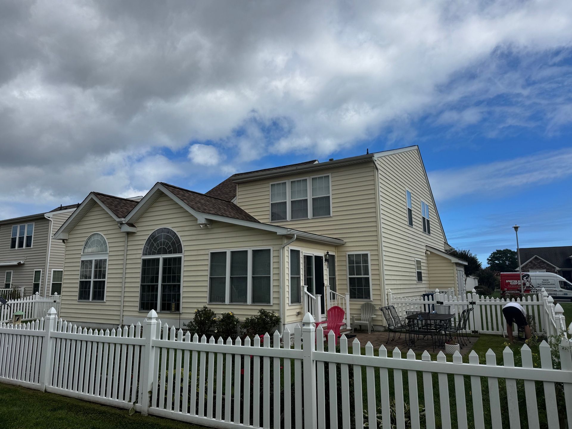 Cream-colored suburban house with white picket fence under a cloudy sky