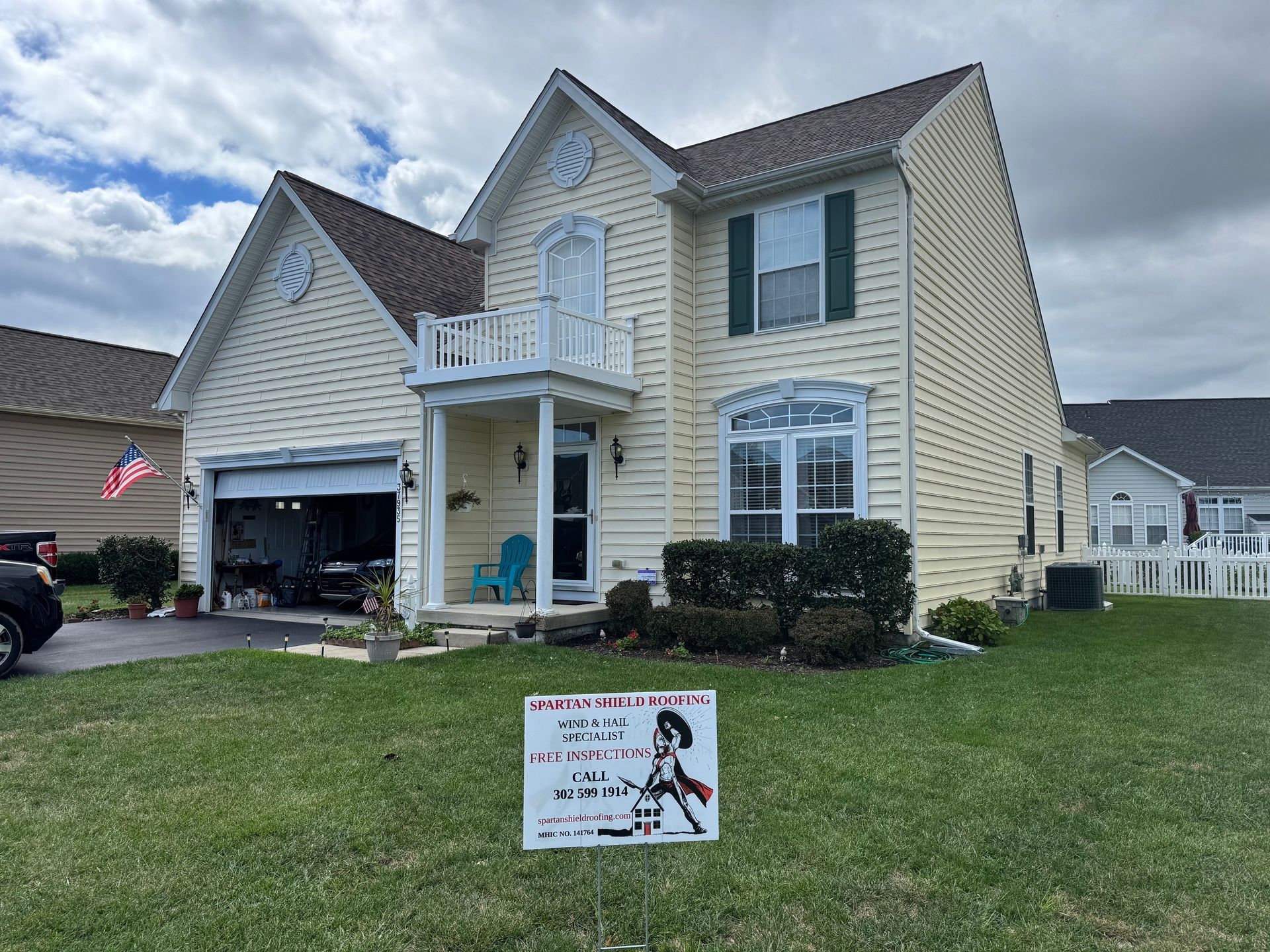 Two-story beige house with blue trim, open garage, and a lawn sign in front.