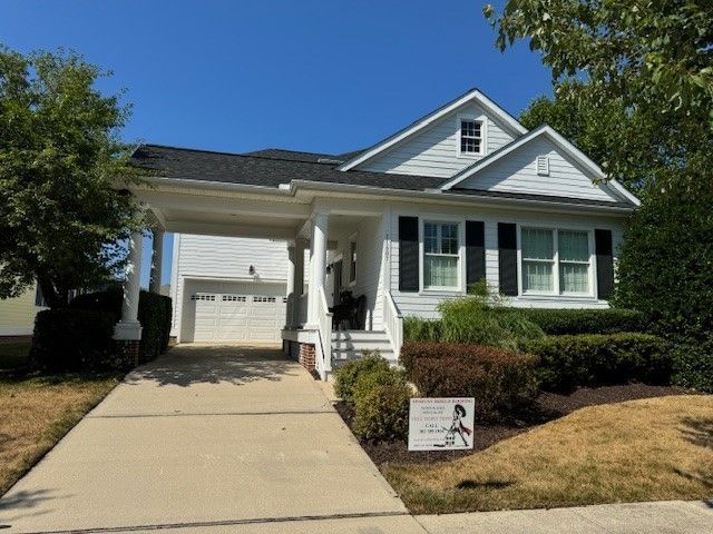 White house with a front porch, garage, and driveway, with a small lawn sign in front.