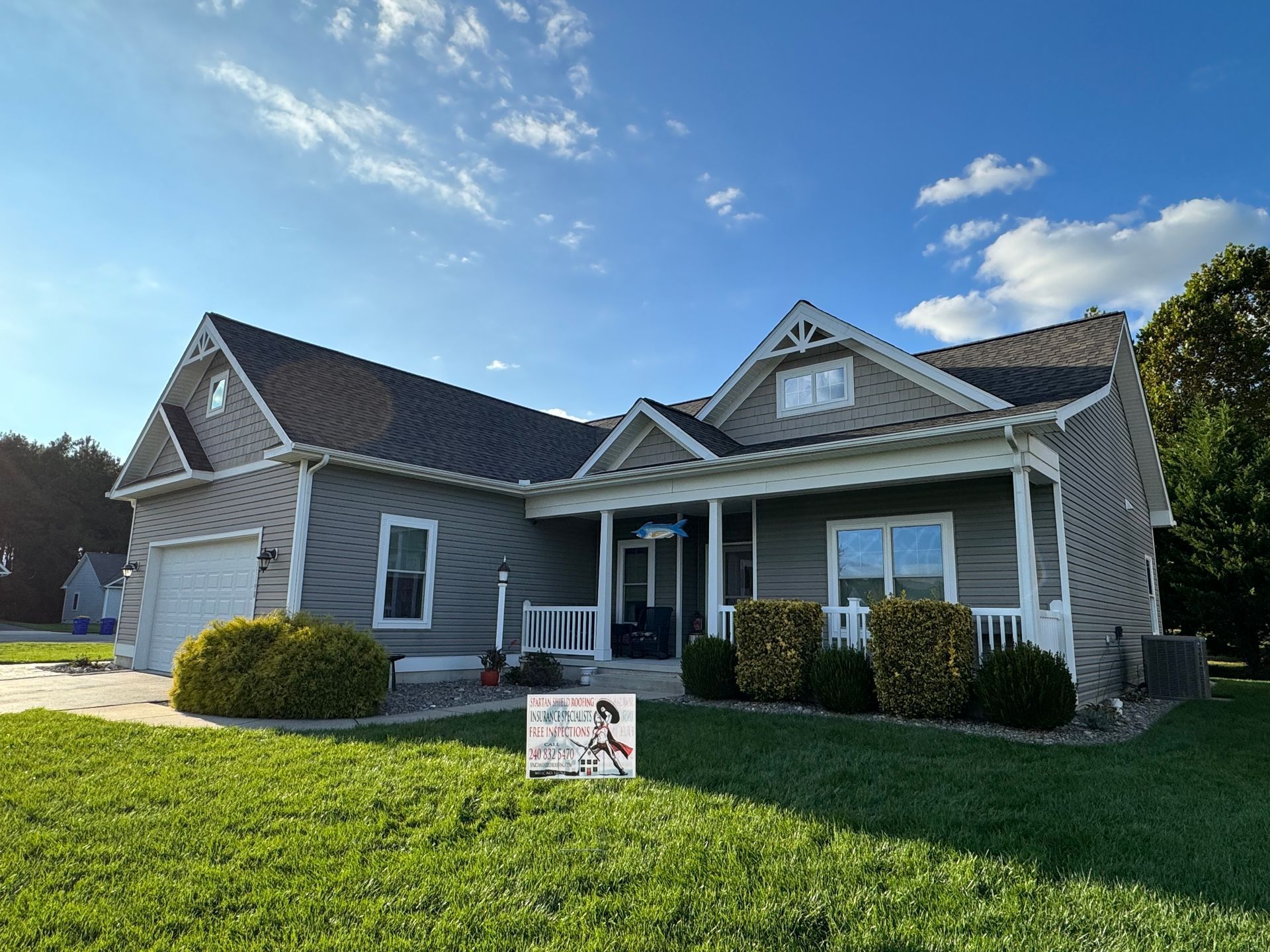 Suburban gray house with manicured lawn and blue sky on a sunny day