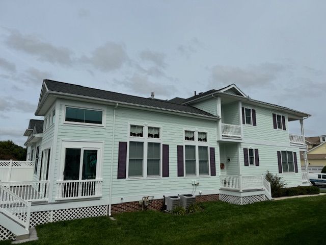 Large pale green two-story house with white trim and porch on a grassy hill