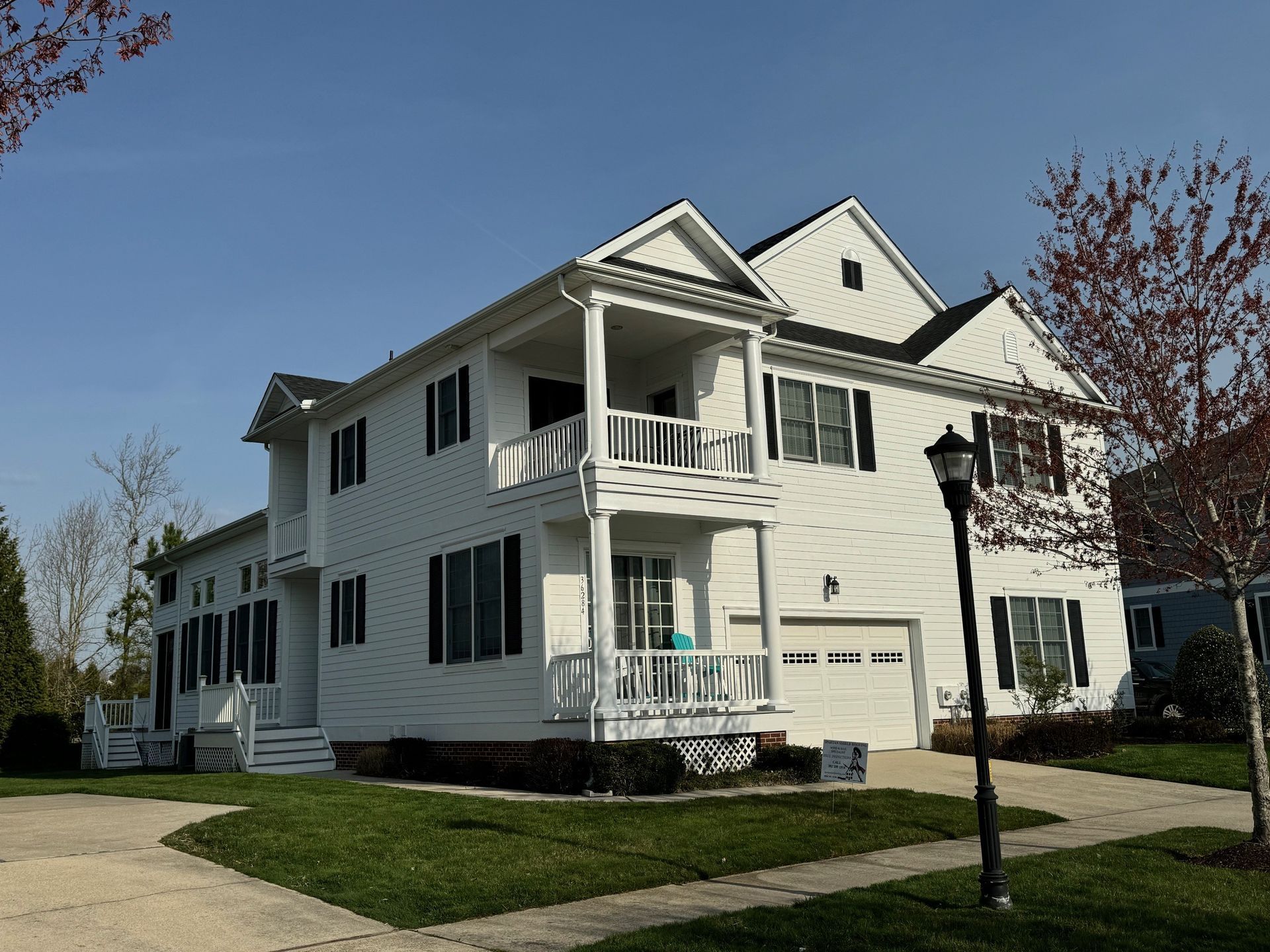 White two-story house with balconies and garage on a sunny suburban street