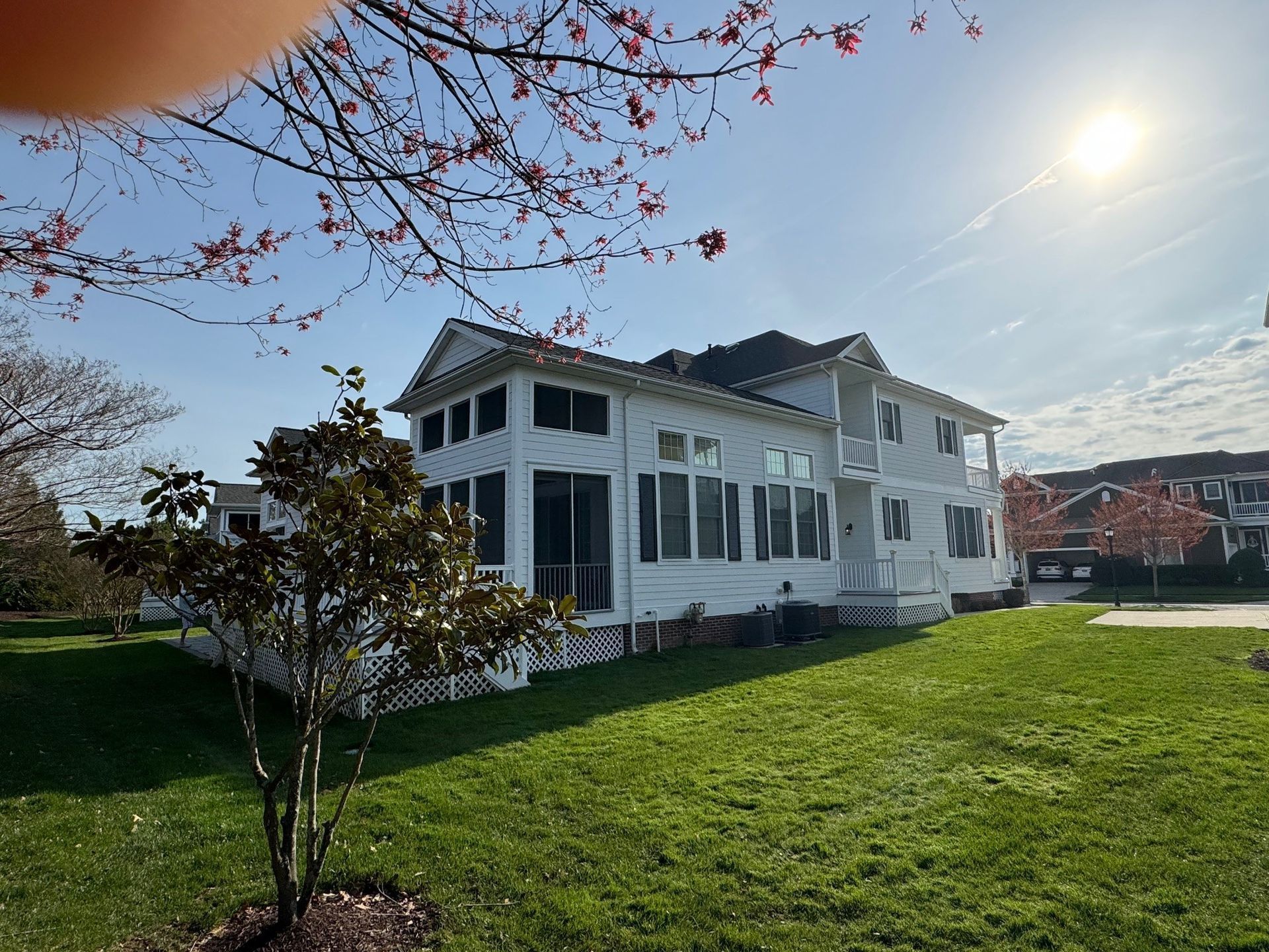 White two-story house with large windows beside a green lawn under a bright sunny sky
